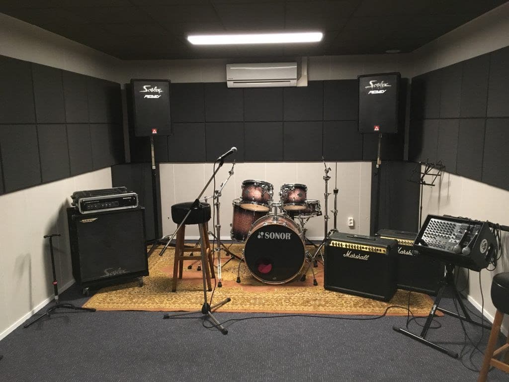 Overzicht van de oefenruimte met drumstel, versterkers, speakers en airco